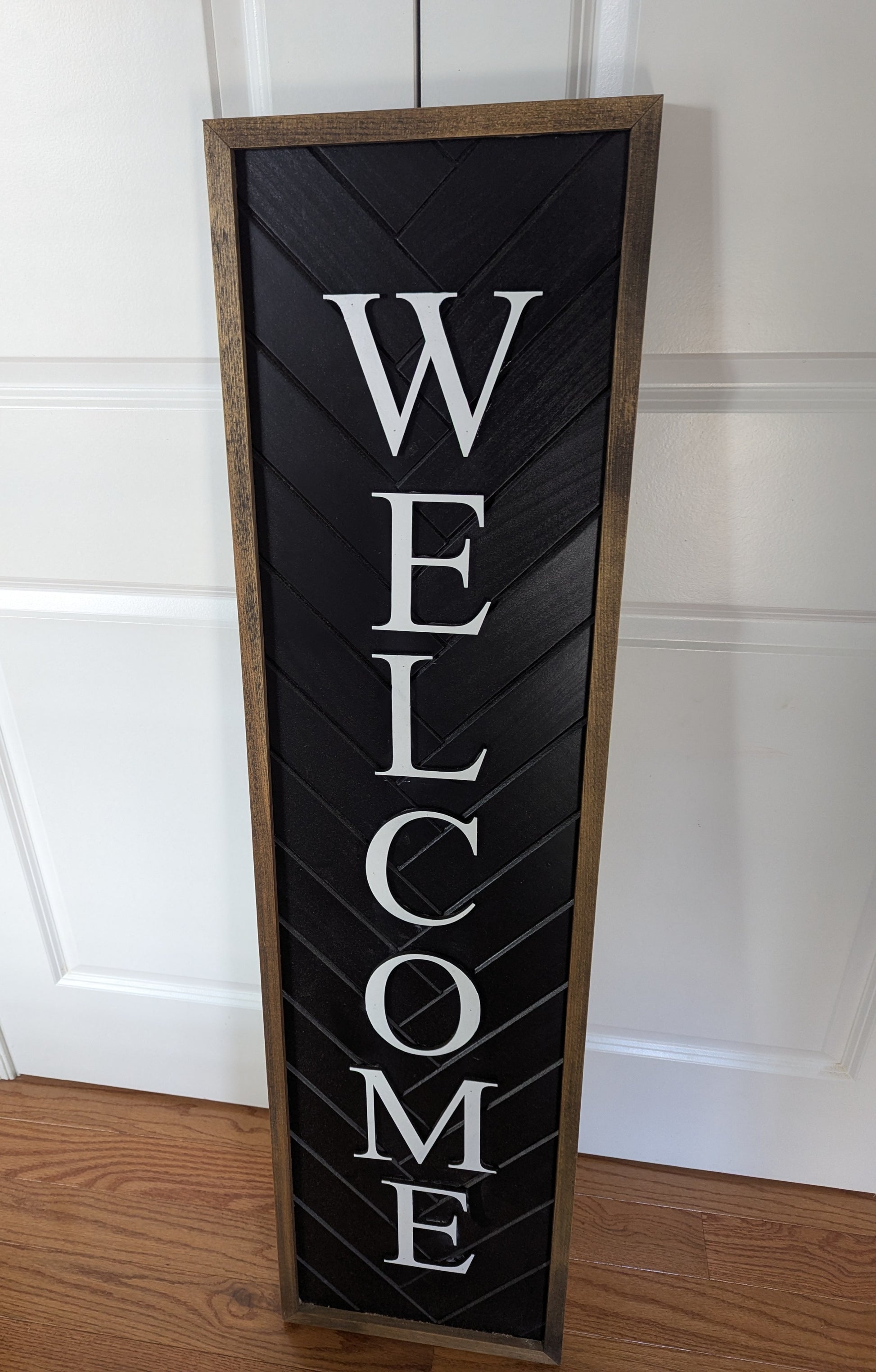 Vertical 'WELCOME' sign with wooden frame on a white wall.